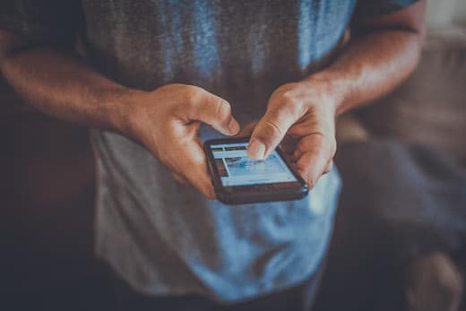 Benefits Handykostenzuschuss | Mann mit grauem T-Shirt hält Handy in der Hand und benutzt Social Media
